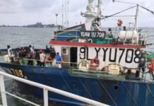 Chinese Fishing Vessel Rescues Five Sierra Leonean Fishermen After Boat Sinks Blue fishing boat moored at a pier, with large white registration numbers along the hull and several people on the deck against a water backdrop.