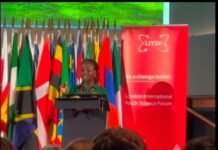 From UBA Essay Competition to Imperial College: Sherilyn Kamara Takes Sierra Leone to Global Stage Female speaker at a podium addressing an audience, with international flags behind and a red London International Youth Science Forum banner on stage.