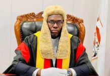 Speaker Urged to Summon Police Cybercrime Unit Over Rising Online Fraud Judge in a black, red, and gold robe sits at a desk in a courtroom wearing a traditional beige wig and white gloves.