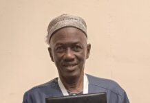 Independent Observer Managing Editor Honoured at 2nd Annual Scholar Media Africa Conference in Nairobi Man in a traditional cap and blue tunic holds a black award plaque titled 'MEDIA EXCELLENCE AWARD' and smiles at the camera.