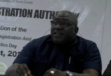 NCRA Commemorates 9th Africa Civil Registration and Vital Statistics Day A bald man with glasses in a navy shirt sits at a table handling papers at a registration event backdrop.