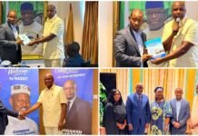 Fuaad Daboh Hands Over NASSIT Leadership to New Director General Chernor Mamoud Jalloh Two men in suits shake hands on stage as one presents a certificate, with a large portrait in the background and a table nearby.