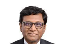 VIKSIT BHARAT 2047: A ROADMAP TO BECOME A DEVELOPED NATION Portrait of a man in a pinstripe suit and patterned tie, wearing black-rimmed glasses, against a white background.