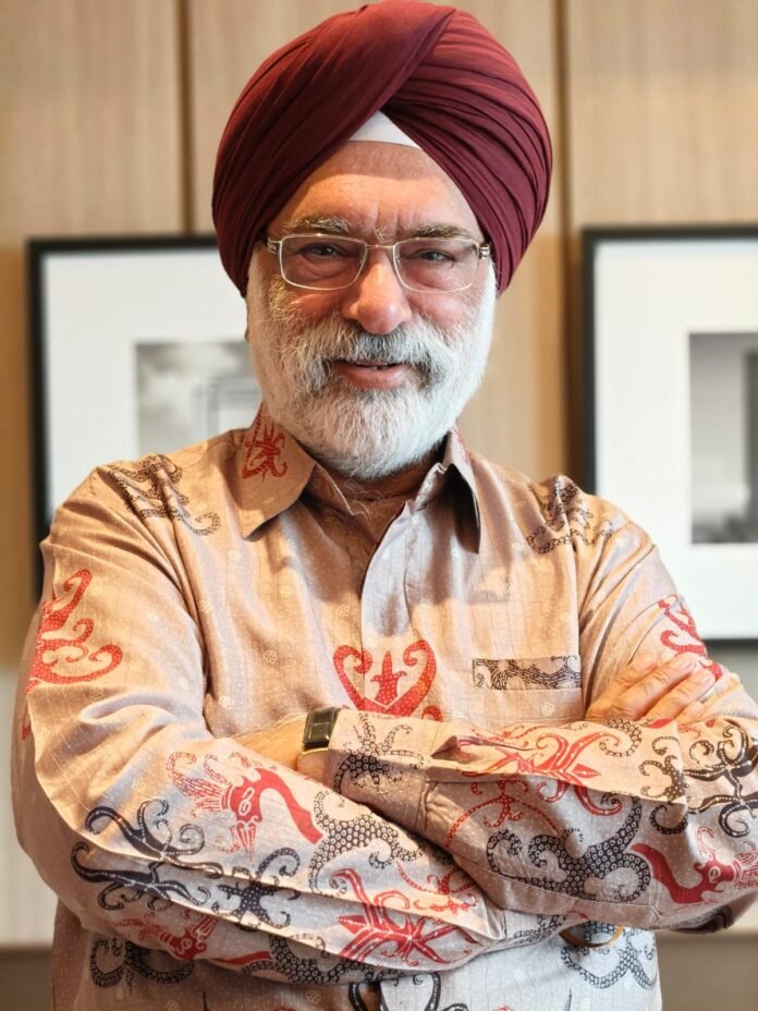 Portrait of a smiling Sikh man with a maroon turban and glasses, arms crossed indoors.