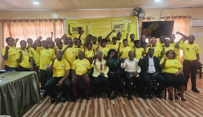 Large group of Amnesty International volunteers posing together in a room, all wearing yellow shirts and raising their fists in solidarity.