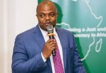 CHRDI Warns Parliament Against Bypassing Constitutional Safeguards Professional man in a blue suit speaking into a microphone at a podium, with a green backdrop behind him.