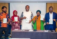 New FAJ Publication Amplifies African Voices in Global Just Transition Debate Five diverse presenters stand behind a conference table on a stage, each holding a booklet or report and smiling at the camera.
