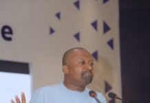 VP Embarks on Regional Tour to Strengthen Local Governance and Deepens Decentralization Man in a light-blue traditional outfit speaks at a wooden podium with two microphones, gesturing with his hands.