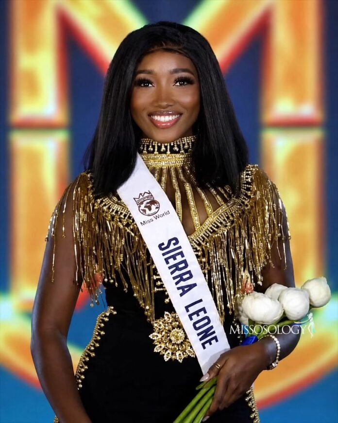 Miss World contestant from Sierra Leone in a gold, beaded dress with a white sash, smiling on stage and holding a bouquet of white roses.