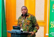 Hon. Marray-Conteh Advocates Stronger Cyber Defences Without Restricting Free Expression Man in a colorful patterned shirt stands at a podium delivering a talk at a conference, with green banners behind him.