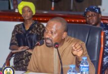 Vice President Launches Nationwide Decentralisation Consultations in Kenema, Bo to Strengthen Local Governance Man in brown traditional attire speaks into two microphones at a desk, with water bottles and a seal emblem visible on the table, inside a formal meeting room.