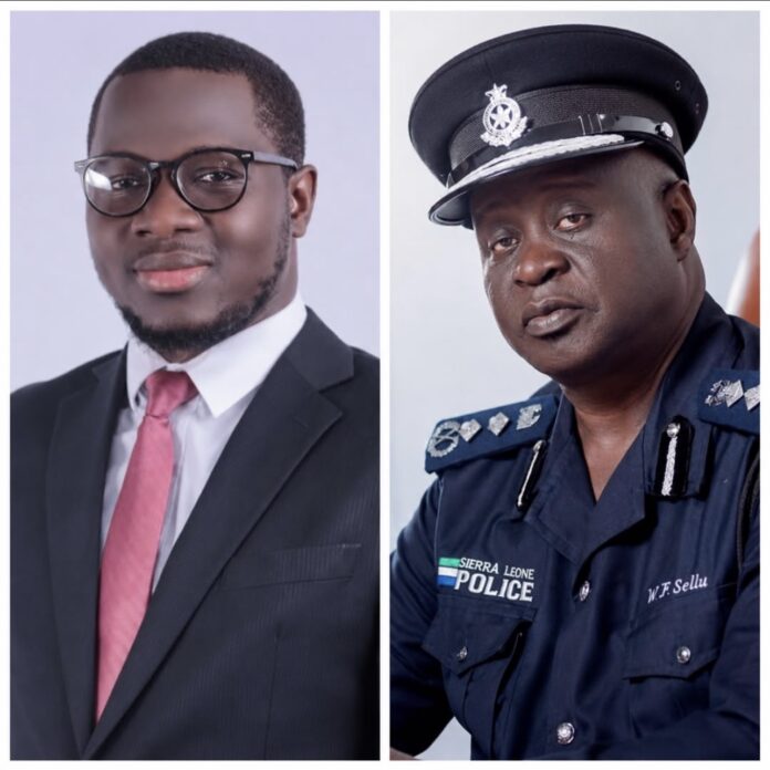 Two men photographed side by side: left is a young man in a suit with a pink tie and glasses; right is a Sierra Leone police officer in a dark blue uniform and cap.