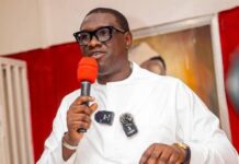 Dr. Ibrahim Bangura Urges President Bio to Withhold Assent Pending Supreme Court Review Man in a white traditional outfit speaks into a bright orange microphone at a stage event, wearing glasses and a wristwatch.