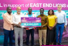 Africell, Afrimoney Boost East End Lions’ CAF Campaign with NLe150,000 Group of six adults posing together, holding a large donation check that reads 'NLE150,000' for East End Lions FC, with logos of Afrimoney and Africell in the background.