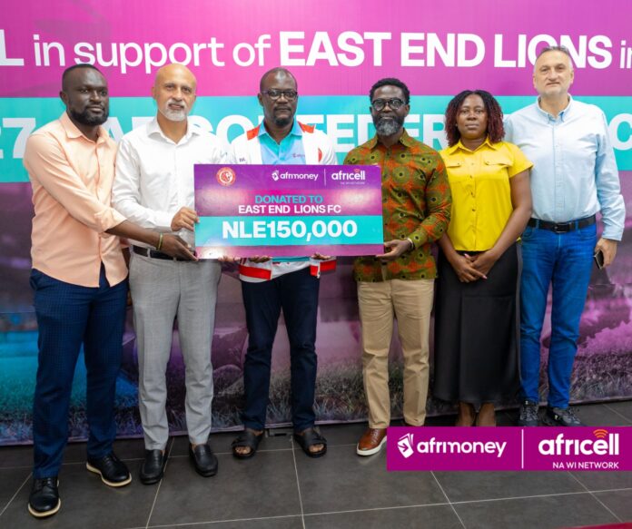 Group of six adults posing together, holding a large donation check that reads 'NLE150,000' for East End Lions FC, with logos of Afrimoney and Africell in the background.