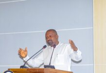 Vice President Calls for Policies That Deliver Meaningful Results for Citizens at National Symposium Man in a white shirt speaks at a wooden lectern with two microphones, gesturing with his hands