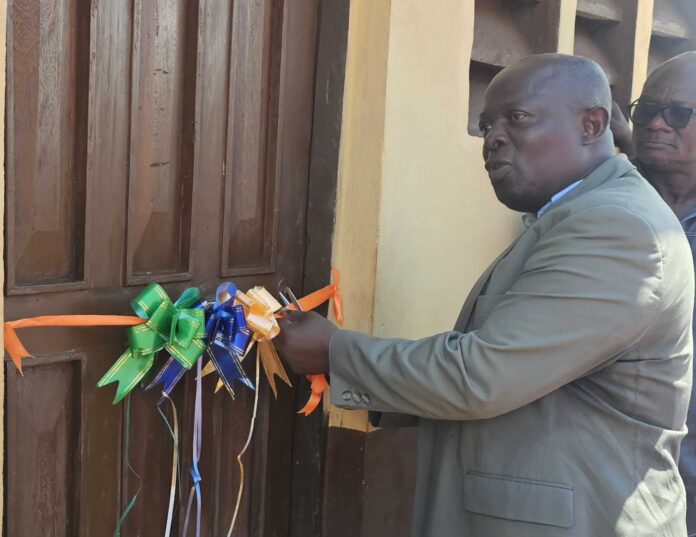Man in a gray suit ties colorful bow ribbons to a wooden door, likely for a ribbon-cutting or decoration event.