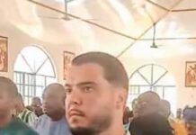 ONS Confirms Nationwide Hunt for Suspected Drug Traffickers Umarr Sheriff and Jos Leijdekkers Man with short dark hair and trimmed beard in a white shirt stands in a crowded indoor gathering with arched windows in the background.