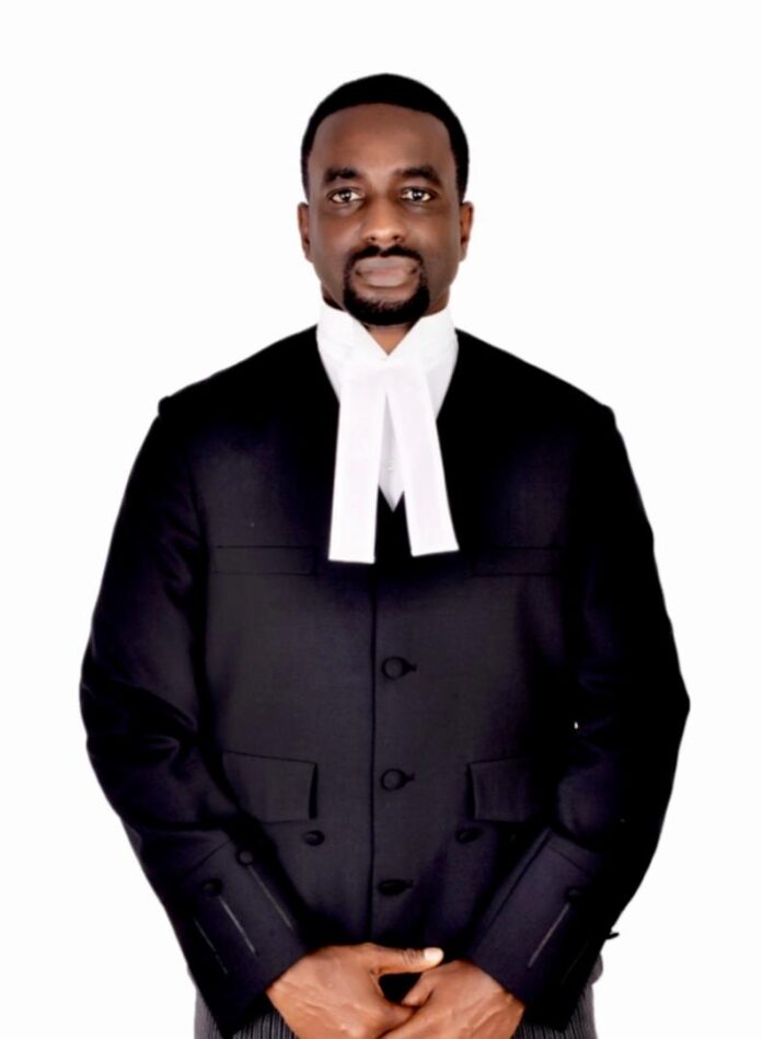 African man in a black barrister's gown with white neck bands, standing with hands clasped in front.