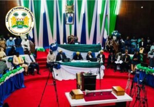 Panel of officials seated at a podium in a formal conference hall, with Sierra Leone flags and the Ministry of Transport and Aviation emblem visible.