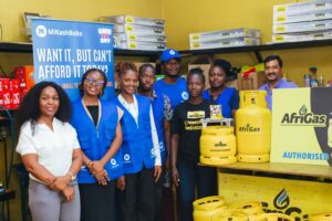Group of people posing in a store with yellow walls and gas cylinders, a banner behind reads 'WANT IT, BUT CAN'T AFFORD IT' and 'Afrigas' logos.