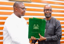 Mohamed Rahman Swaray Assumes Office as Sierra Leone’s Foreign Affairs Minister Two men shake hands while one hands over a green folder with the Sierra Leone crest, in a formal setting.