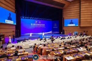 Large conference hall with a blue-lit stage and two podiums; audience seated, banners show Sierra Leone's Ministry of Information and Civic Education (forum setting).