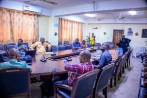 | The Calabash Newspaper Group of professionals seated around a large conference table in a meeting room, with laptops and a photographer filming in the background.