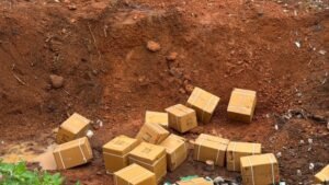 Cardboard boxes with packing tape scattered in a muddy dirt trench or excavation area.