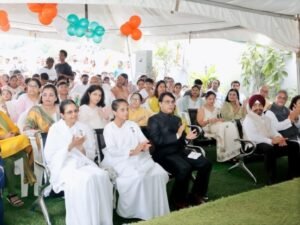 Audience seated under a white tent at a formal event, with balloons and attendees applauding or listening attentively.