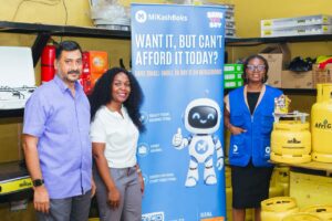 | The Calabash Newspaper Three people pose beside a blue MiKashBoks banner with a friendly robot mascot in a shop with gas cylinders visible behind them.