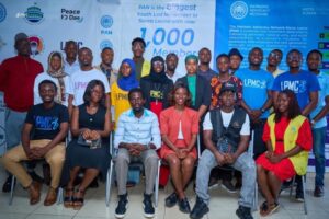 | The Calabash Newspaper Group of diverse young people posing for a photo at a youth movement event, with banners noting 1,000 members in the background.