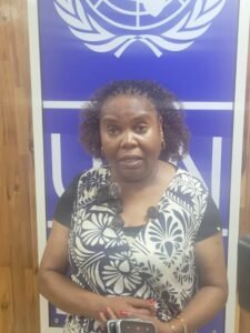 Chairperson of the Public Accounts Committee of the Lesotho Parliament, Honourable Machaba Lemphane-Letsie | The Calabash Newspaper Woman speaking in front of a United Nations banner, wearing a black-and-white floral blouse with a lavalier mic clipped to her top.