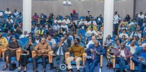 | The Calabash Newspaper Audience in a conference hall, rows of blue seats filled with diverse professionals and cameras set up on stands.