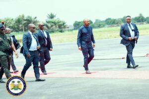 Group of men in suits walking on an airport tarmac with a government seal visible in the bottom-left corner