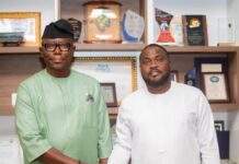 NaCSA Commissioner Praises SLPHA for ‘Remarkable Transformation’ at Freetown Port Two men in traditional outfits shake hands in an office with awards and certificates on shelves behind them.
