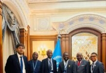 Attorney-General Engages UNESCO on Sierra Leone’s AI Governance Agenda in Riyadh Six men in suits stand together in a gilded, ornate room with a United Nations flag behind them.
