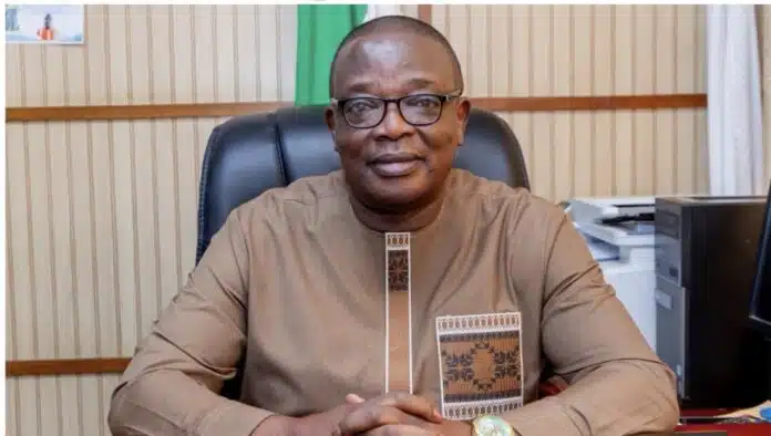 Portrait of a man wearing a brown traditional shirt and glasses, seated at an office desk and looking at the camera.
