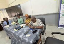 Government Urges UASA to Continue Dialogue as Strike Notice Looms Five people seated at a long table in a conference room, with papers and mugs on the table, one man signing a document as others watch.