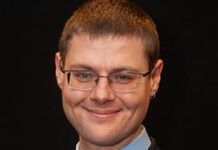 SIERRA LEONE’S NATIONAL AI STRATEGY SHOULD SET AUTHORITY LIMITS FOR AGENTS Smiling man in a dark suit with a blue shirt and tie, wearing glasses, against a black background.
