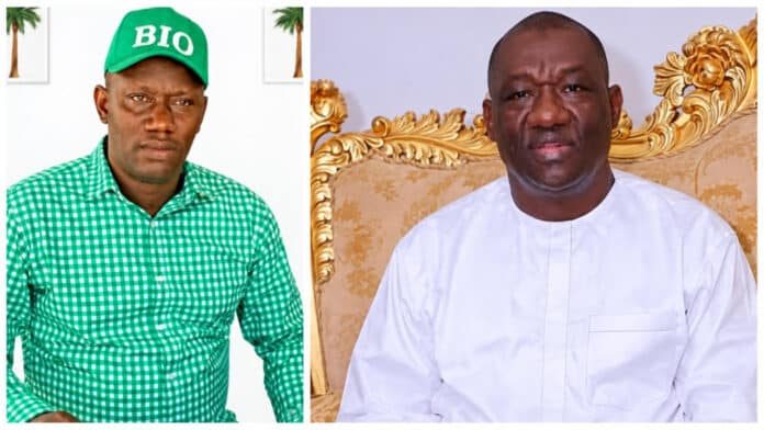 Two men posing for a photo: left man in a green checkered shirt and a green BIO cap, right man in white traditional attire seated on a gold ornate chair.