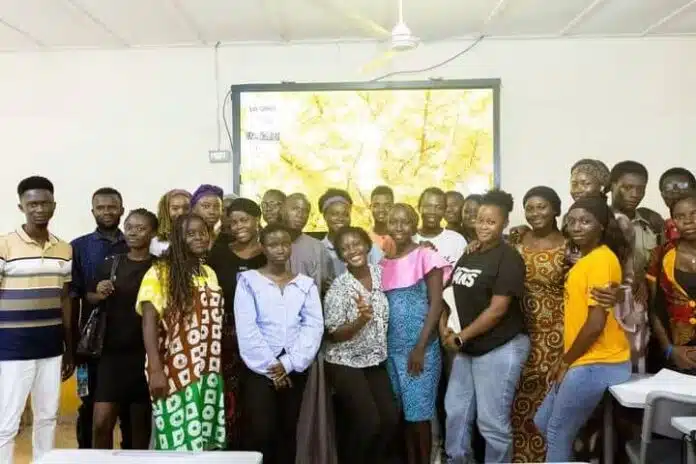 Group of people posing for a photo in a classroom or training room, with a large map projected on a screen behind them and a bright, well-lit setting.