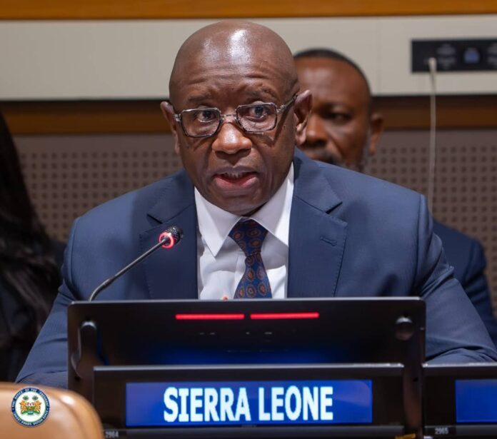 Sierra Leone delegate speaking at a conference podium with a blue nameplate reading 'SIERRA LEONE' and a microphone in front of him