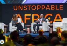 At UNSTOPPABLE AFRICA 2026: President Bio Urges Africa to End Raw Mineral Exports and Expand Local Processing Two panelists on stage in conversation at a conference, with a large UNSTOPPABLE AFRICA banner behind them and an audience in the foreground.