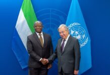 UN Secretary-General Commends Bio’s Leadership, Discusses Africa’s Representation, Regional Stability & Investment Two men in dark suits shake hands in front of Nigerian and UN flags at a formal meeting setting.