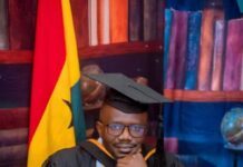 Professor Duramany-Lakkoh Urges Management Accountants to Shape Strategy Beyond the Numbers at 2026 Convocation in Ghana Graduate in cap and gown sits at a wooden desk with a laptop, flag and books in the background.