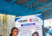 Caritas Freetown Delivers Trocaire-Supported MPCA to Strengthen Disaster Preparedness for 80 Households Two women exchange a small item in front of a project banner about community disaster preparedness and resilience.