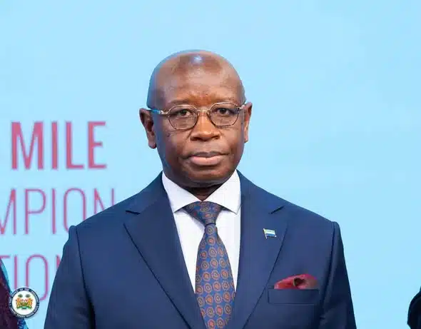 Man in a navy suit and patterned tie stands before a light blue backdrop.