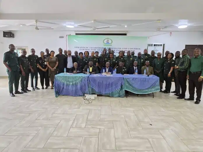 Group of uniformed military officers and civilians posing for a class photo in a conference room, banner behind them reads Strategic Leadership Command and Control Course for Senior Officers.