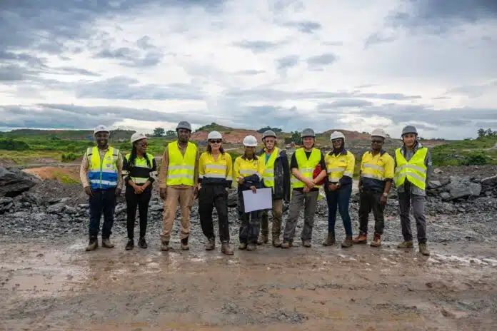 Group of construction workers in neon vests and hard hats standing in a rocky quarry.